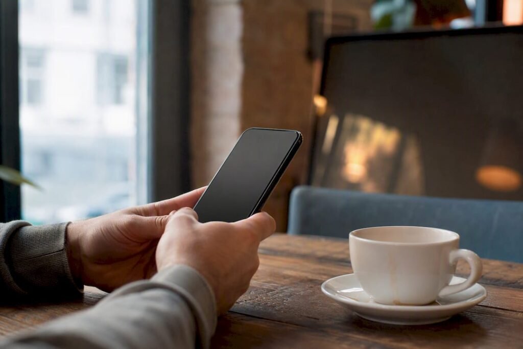 Hände, die ein Smartphone mit dunklem Bildschirm über einem Holztisch halten